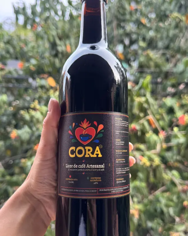 The 700 ml bottle of CORA artisanal coffee liqueur, held up against the coffee field